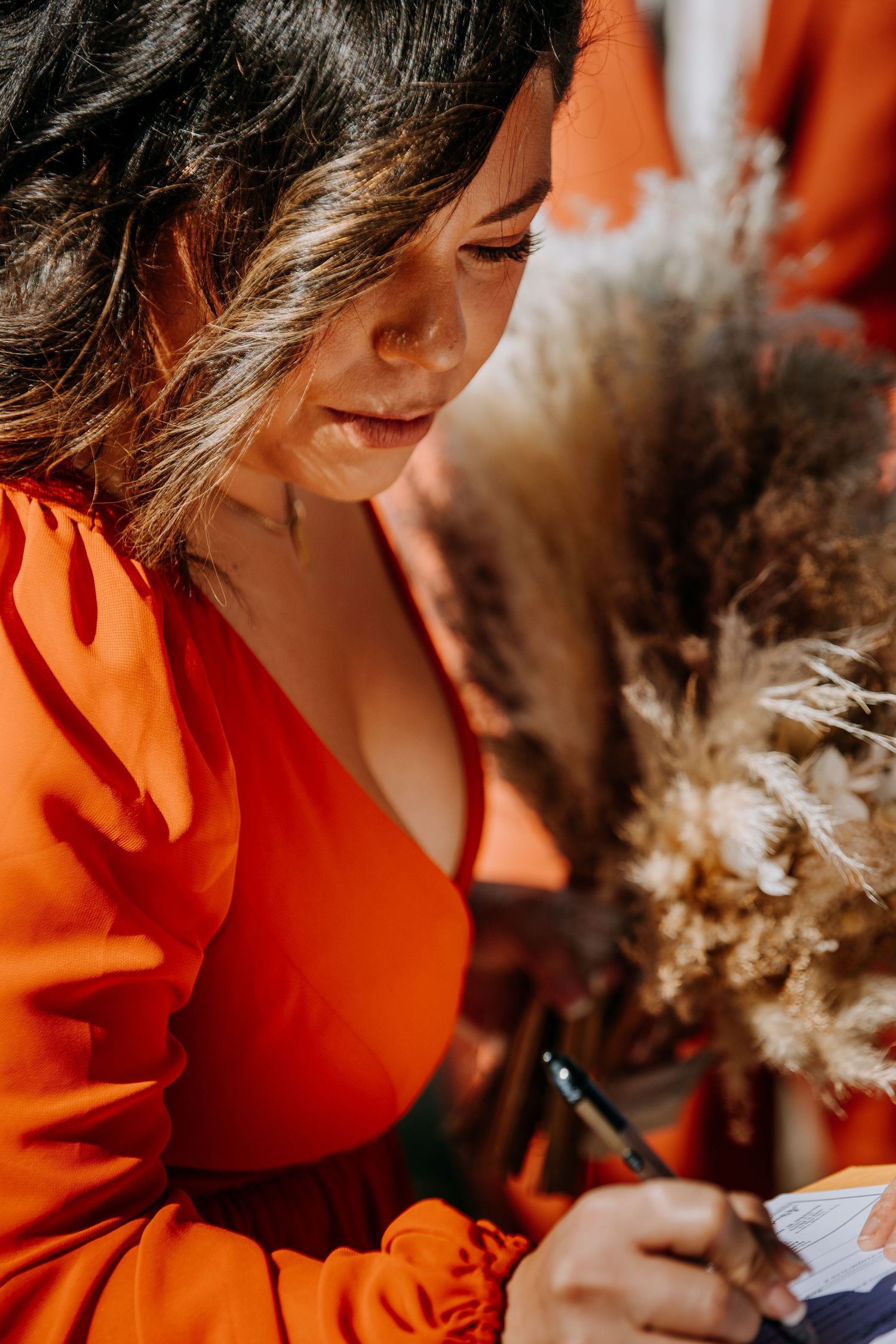 A person in orange writing something while holding dried flowers.