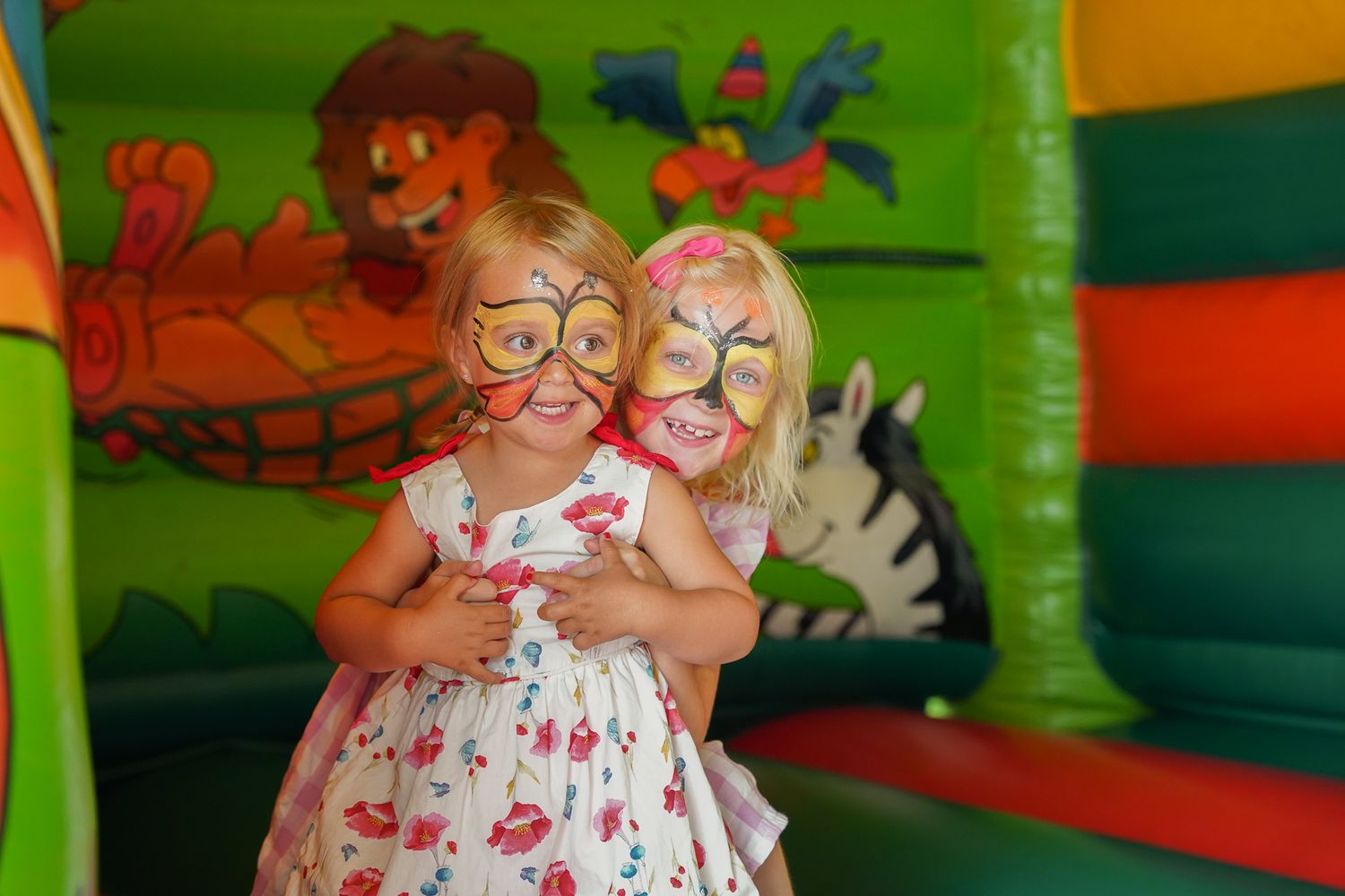 Two children playing together in a colorful indoor bounce house with cartoon decorations on the walls.