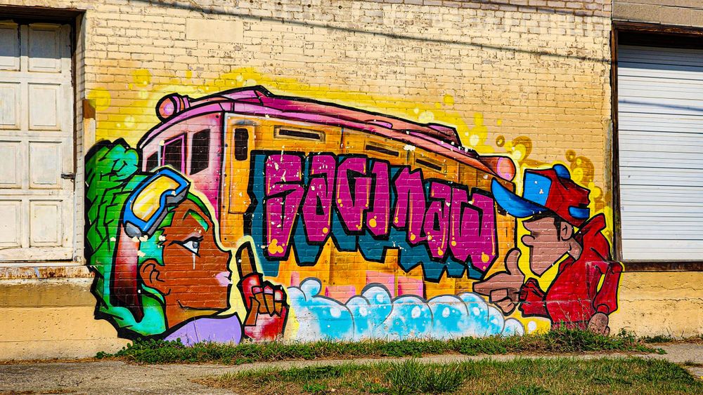 Colorful graffiti art featuring a pink subway train design painted on a yellow brick wall with vibrant characters in Saginaw Michigan.