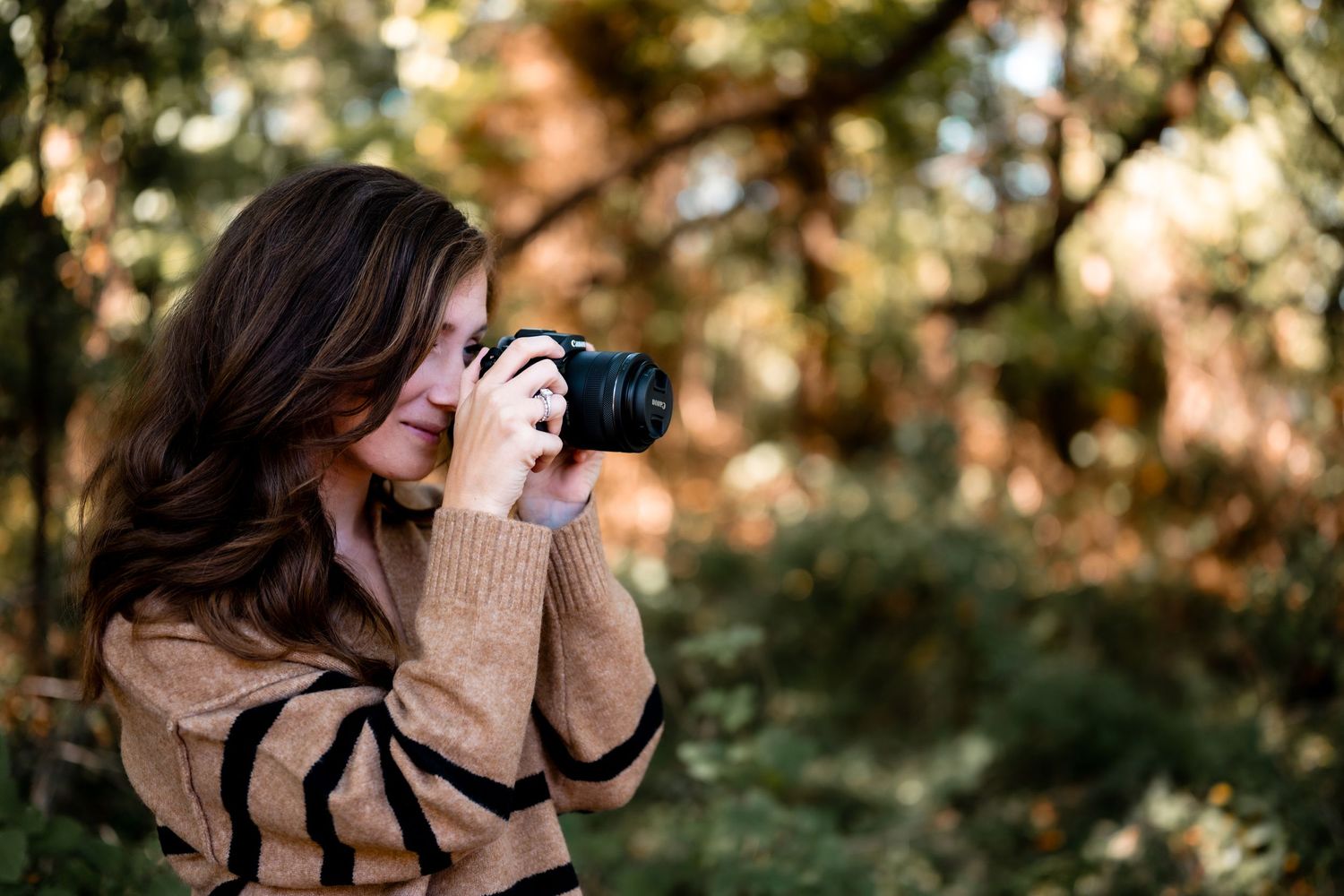 A nature photographer wearing a brown sweater taking photos in a wooded setting.