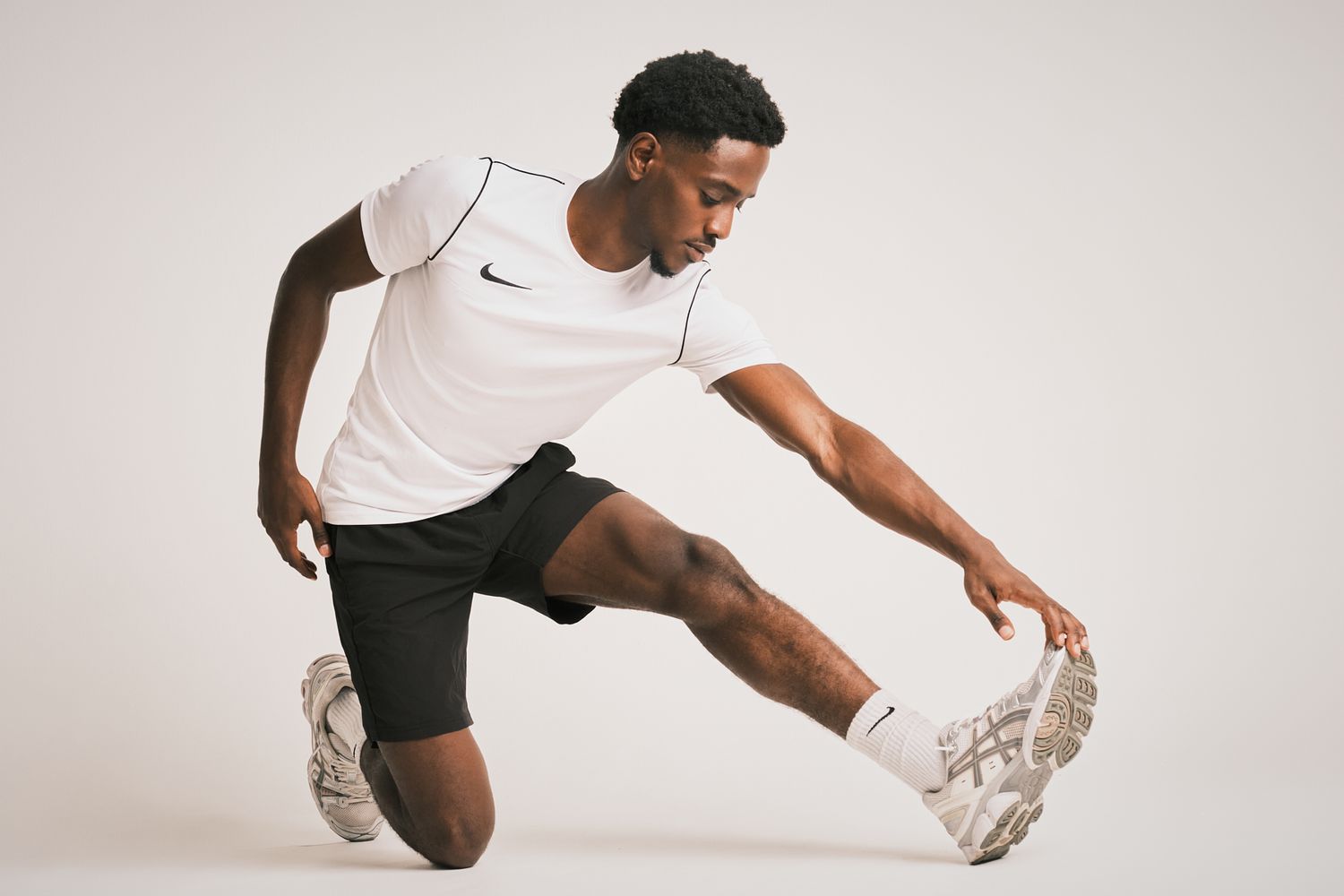 Man in a white Nike t-shirt and black shorts stretching in a studio setting, preparing for a workout