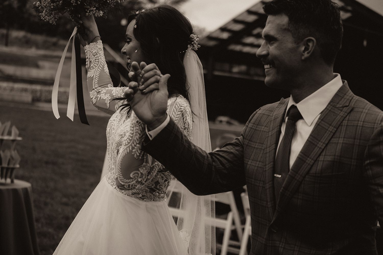 Black and white photo of a bride and groom holding hands at an outdoor wedding ceremony.