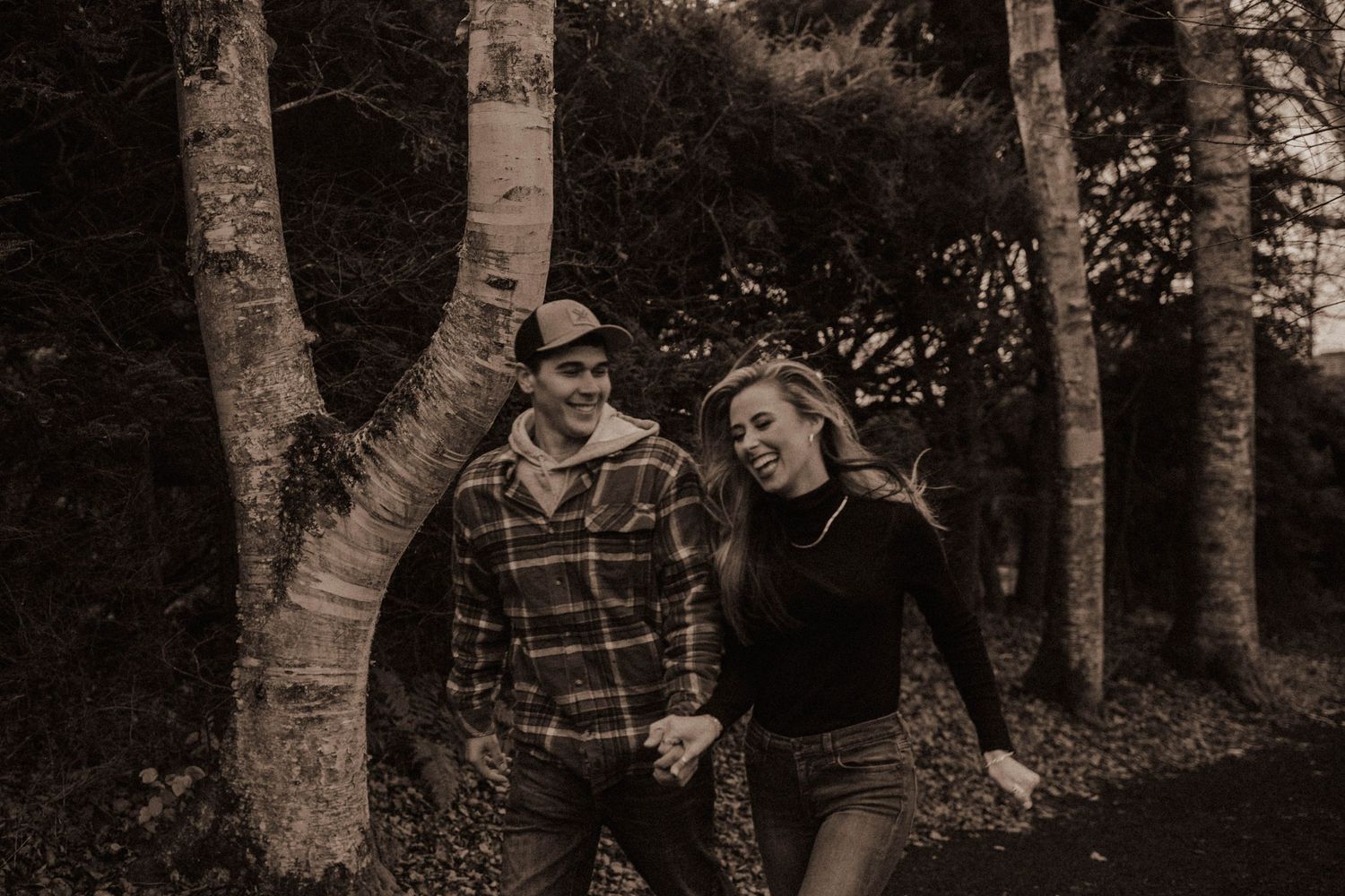 Couple laughing together in black and white photo among birch trees in woods.