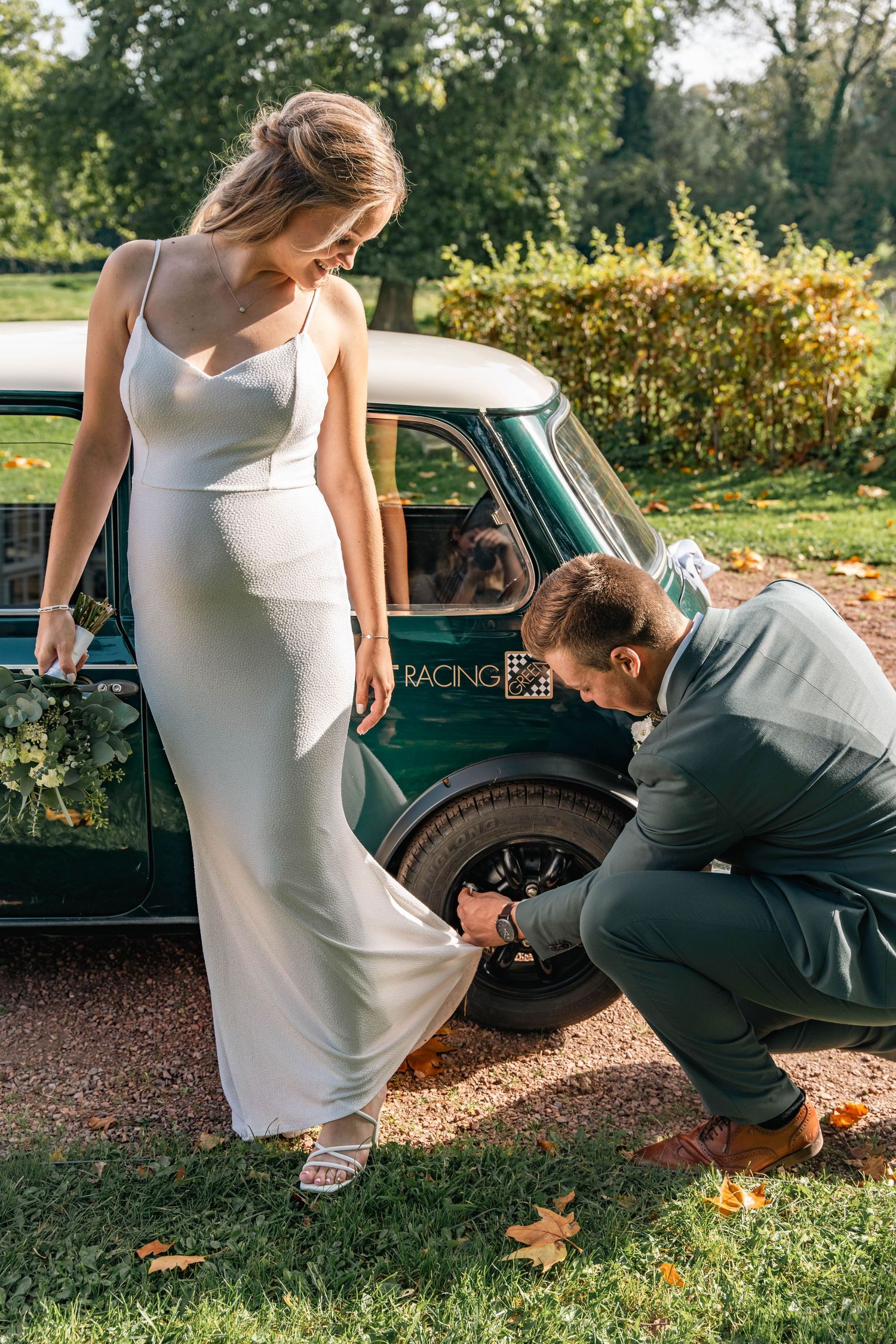 Elegant white dress and vintage green Mini Cooper on gravel path during autumn wedding photoshoot.