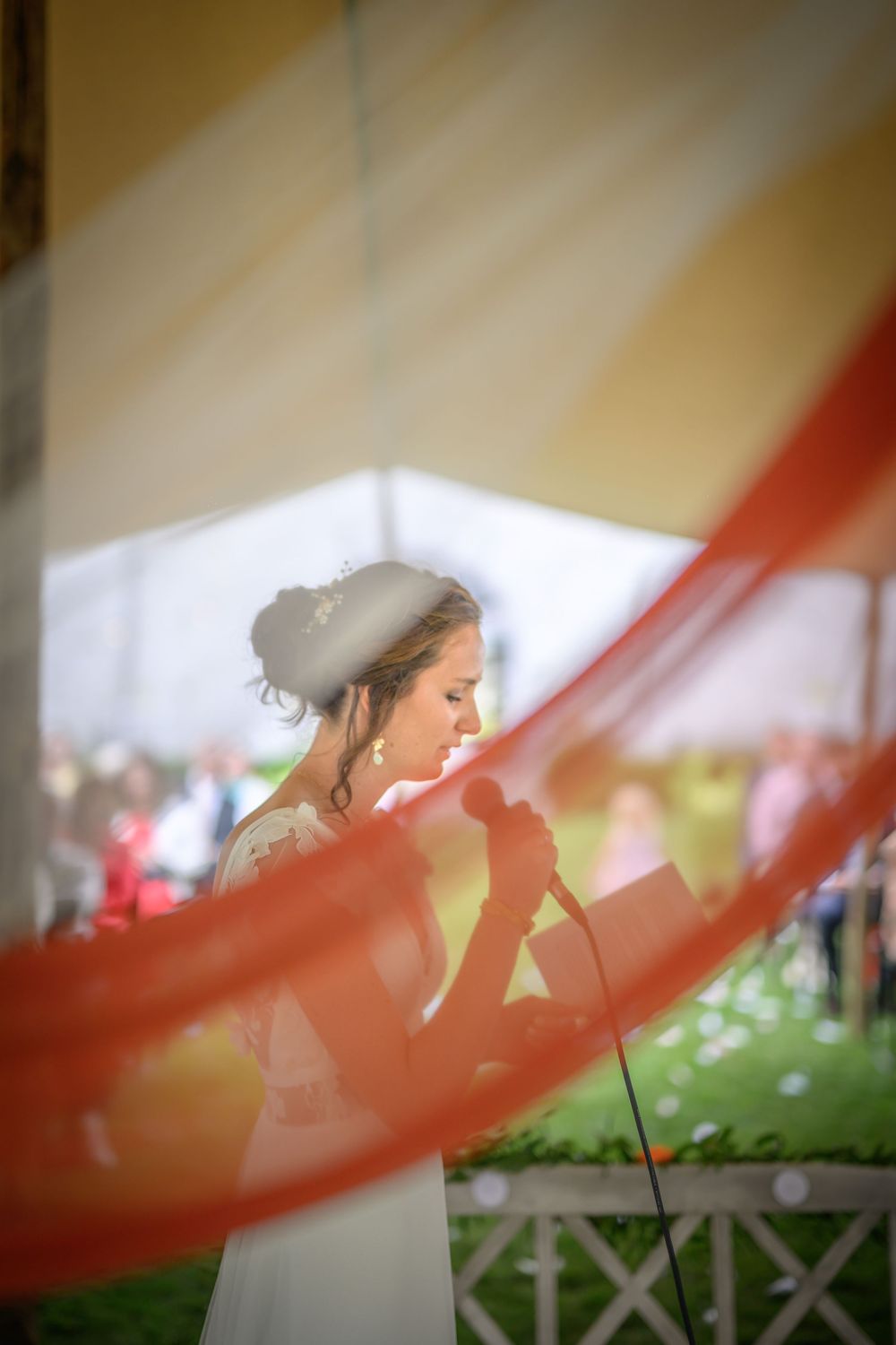 A bride in a white wedding dress stands behind flowing red fabric creating an artistic wedding photograph effect.