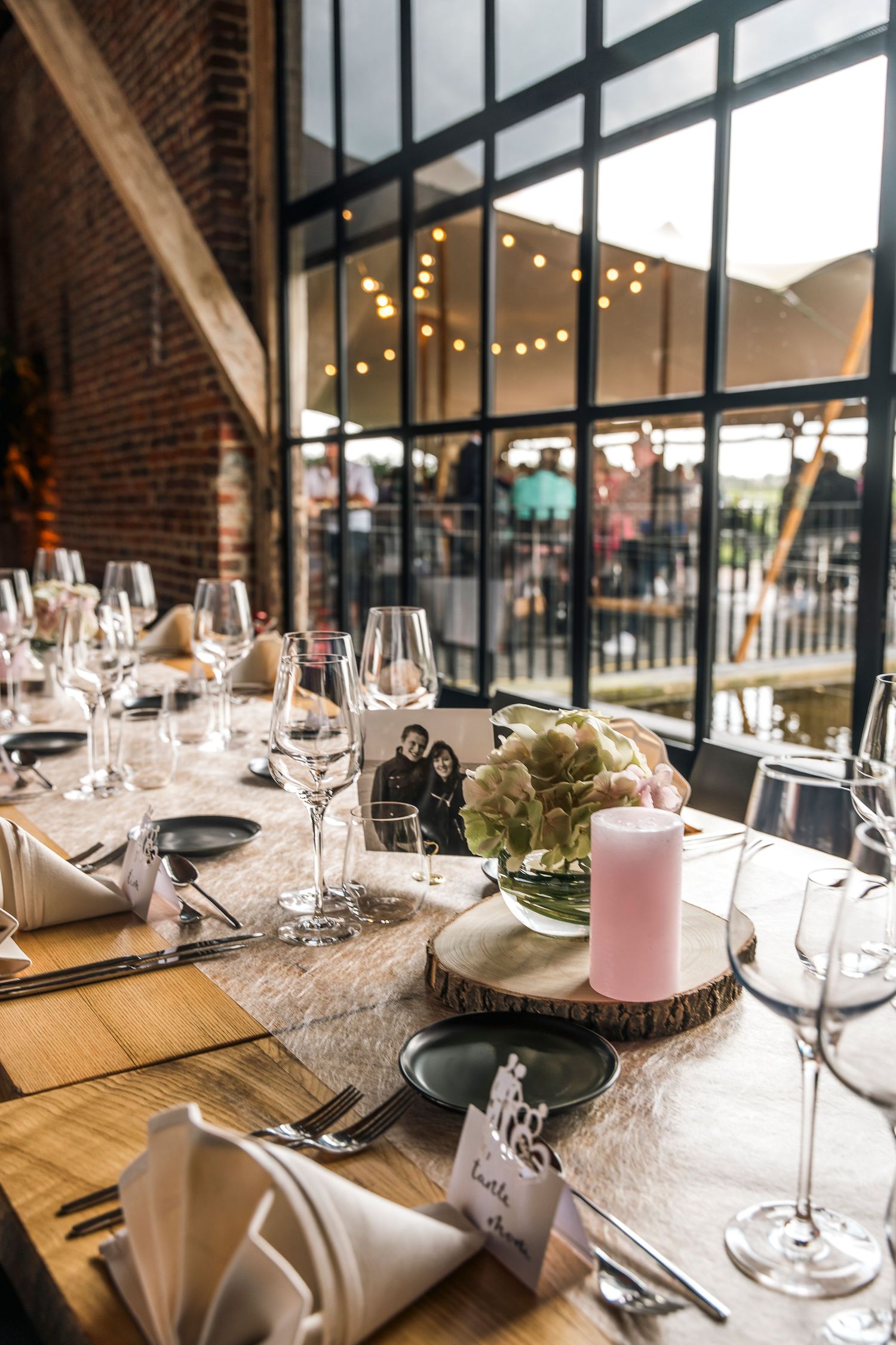Rustic wedding reception table setting with string lights and wine glasses.