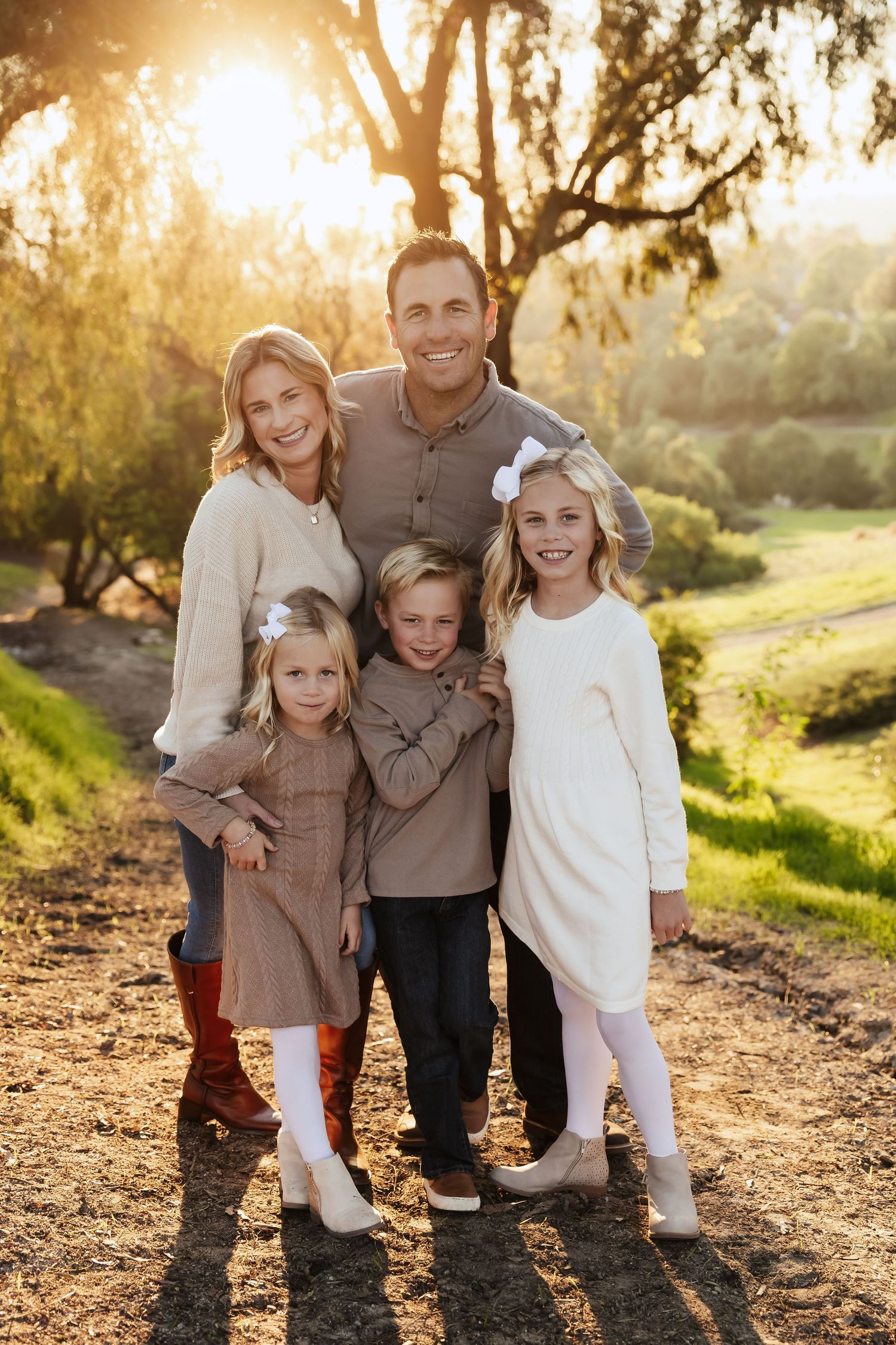 A family of four poses together on a wooden bridge during an outdoor photo session in warm lighting.