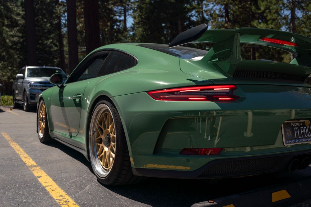 Forest green Porsche 911 GT3 RS with gold wheels parked in mountain setting.