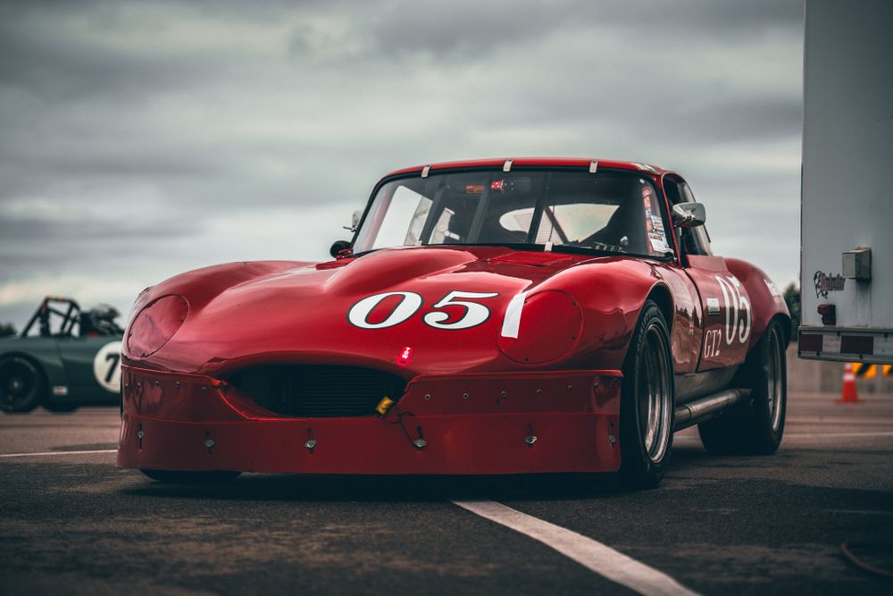 A red vintage racing car with number 05 sits on a race track under cloudy skies.