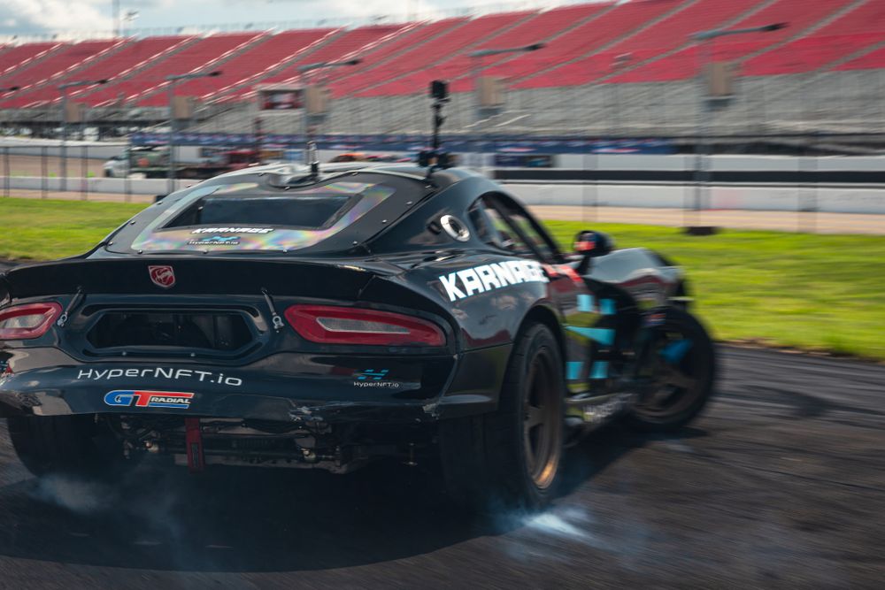 Black sports car drifting on wet track surface with smoke trailing behind.