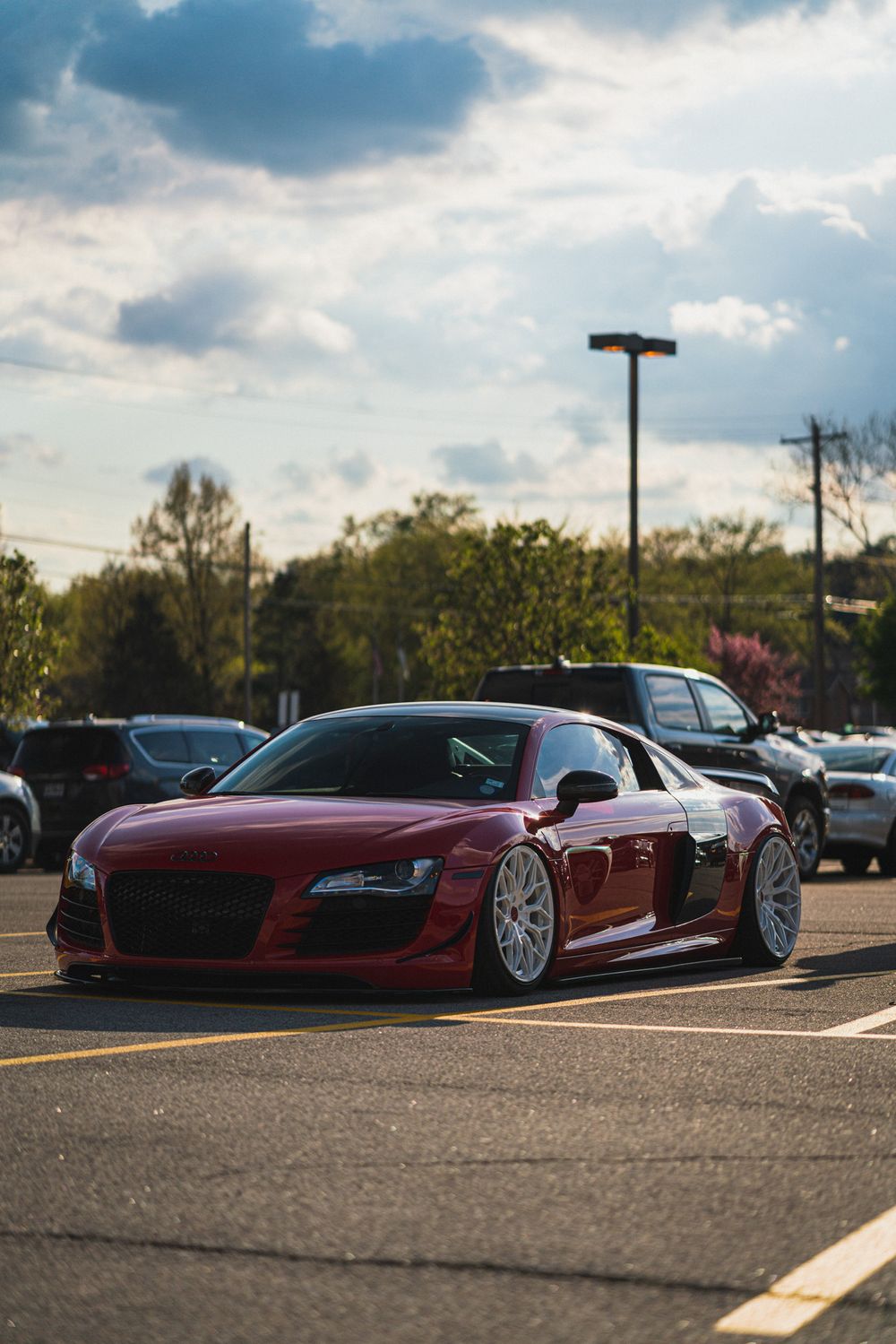 Lowered red Audi R8 with wide body kit parked in suburban parking lot at sunset.