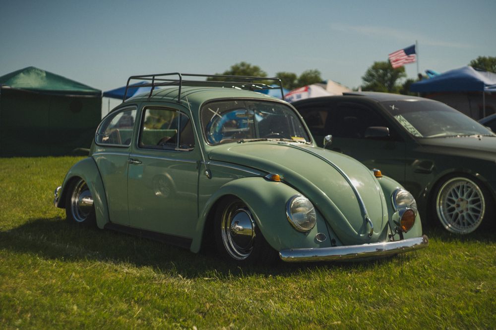 Mint green classic Volkswagen Beetle with lowered suspension on display at car show.