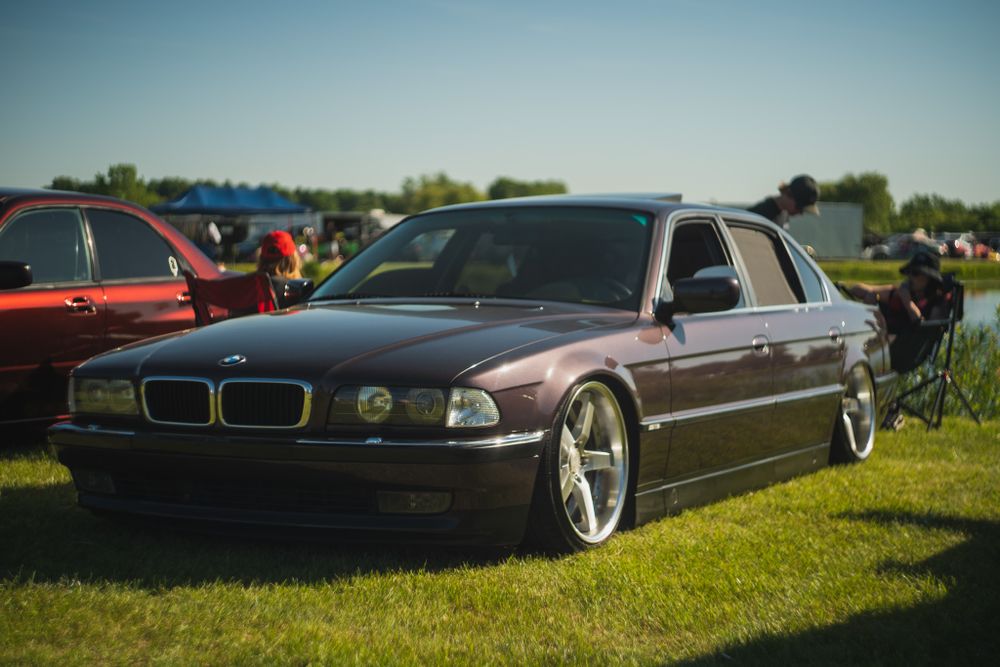 Slammed BMW E38 7-series in metallic brown with aftermarket wheels parked on grass.