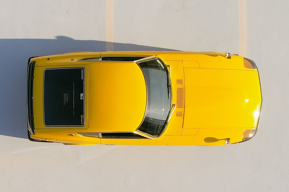 Overhead view of a bright yellow classic sports car against white background.