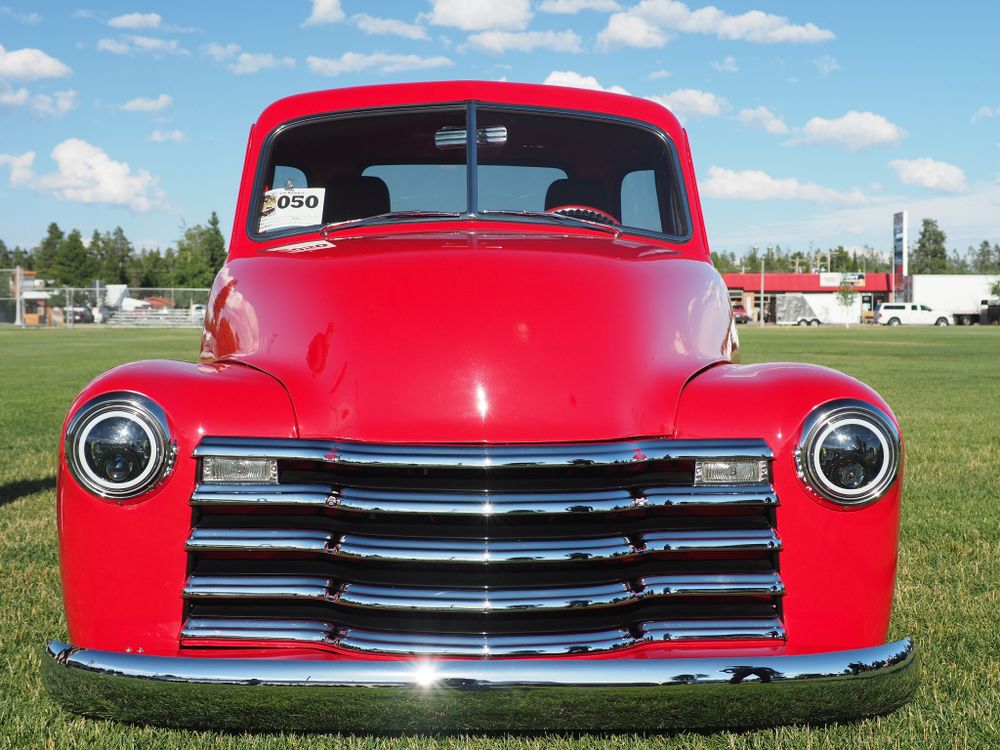 Front view of a bright red vintage Chevrolet pickup truck against a blue sky with chrome grille and round headlights.