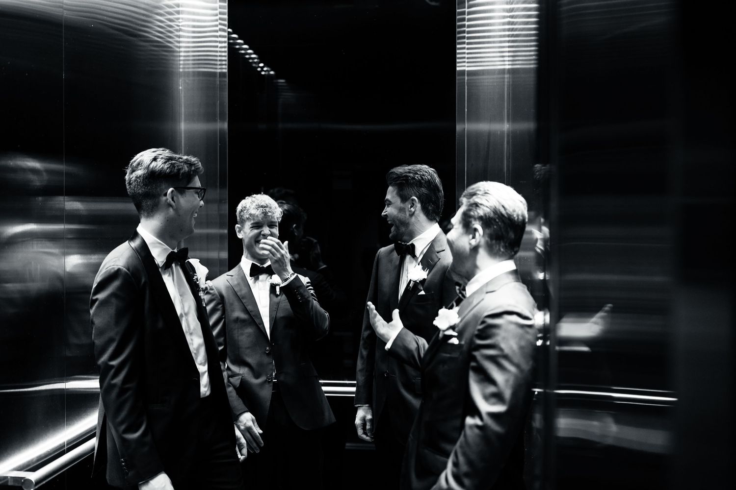 Group of groomsmen sharing a candid moment in a dimly lit elevator.