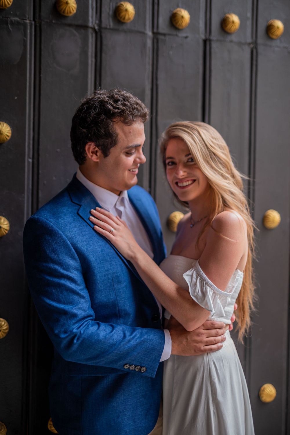 A couple sharing a tender moment against an ornate black door with brass details.