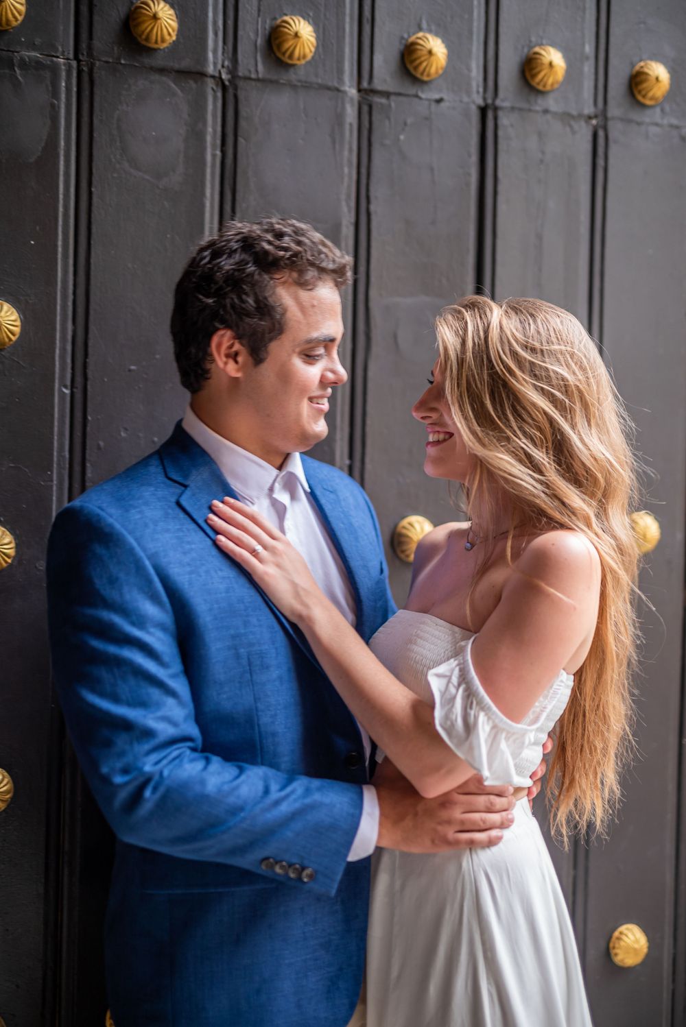 A couple in blue and white attire sharing a loving moment against a dark studded door.