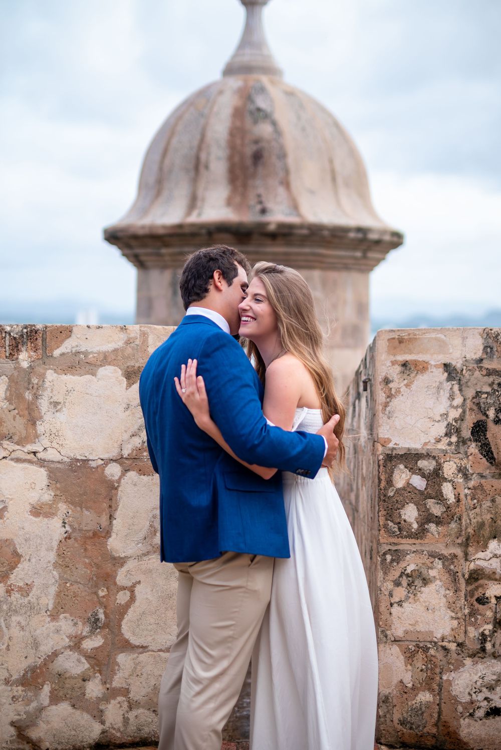 A loving moment shared at a historic fort overlook with dome architecture.