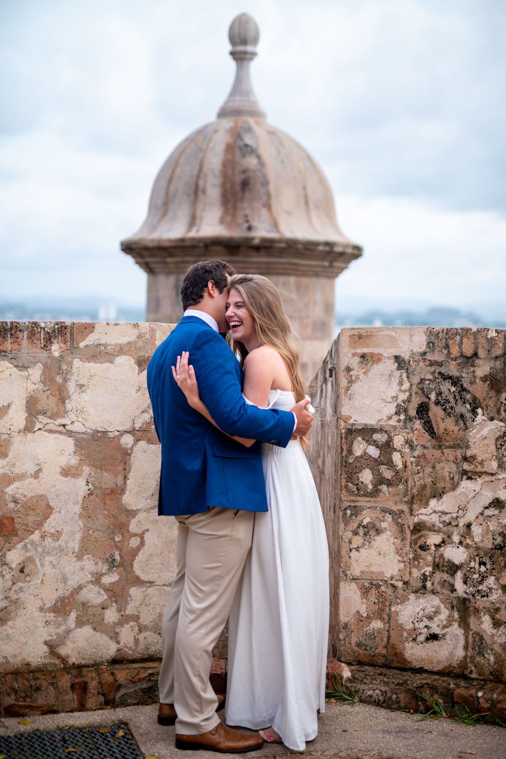 A tender embrace against the backdrop of a stone watchtower and cloudy skies.