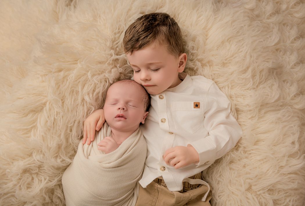 Sleeping baby wrapped in soft cream-colored blanket lying on plush white fur background.