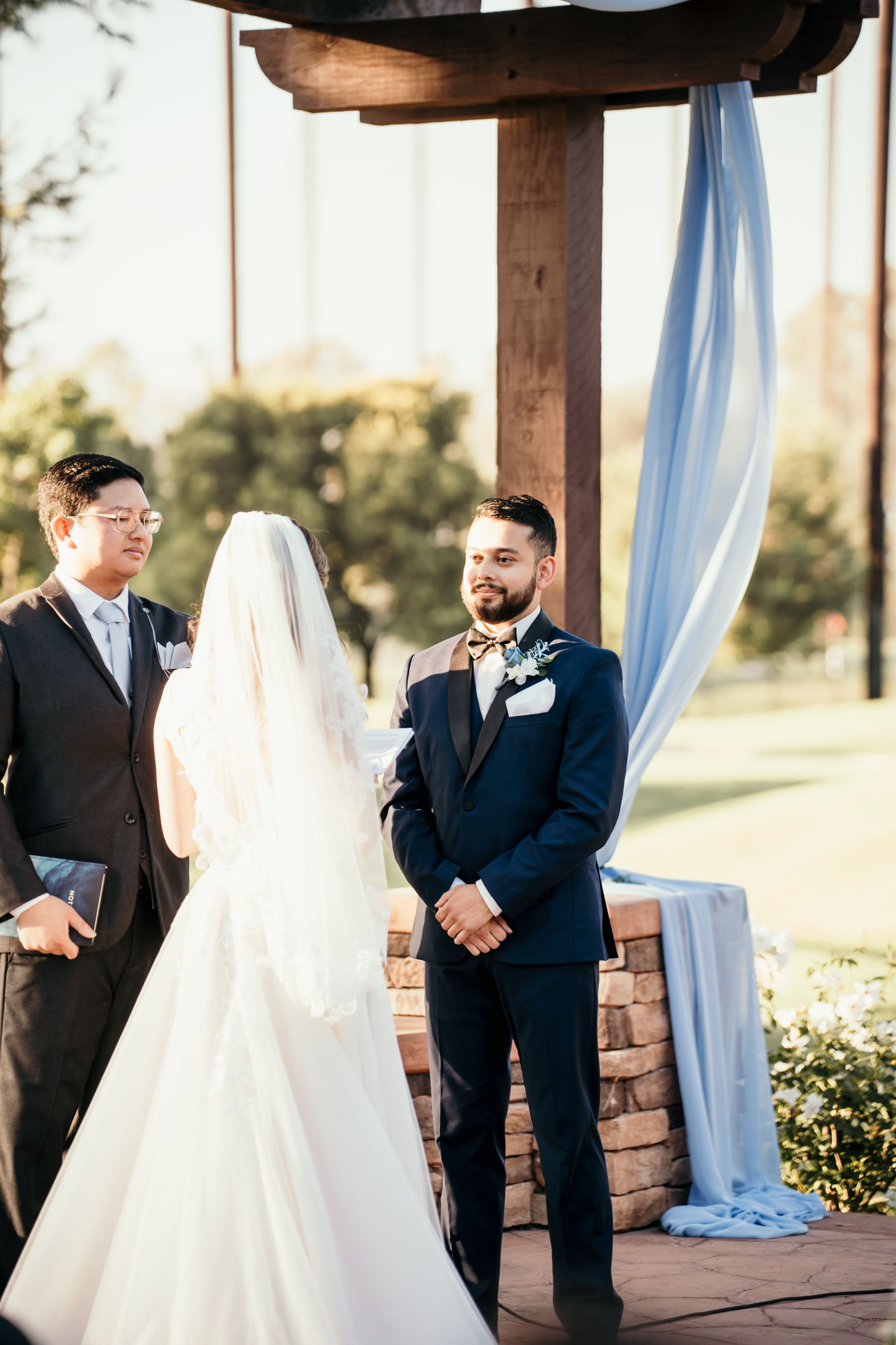Wedding ceremony under a draped pergola with officiant and couple at sunset.