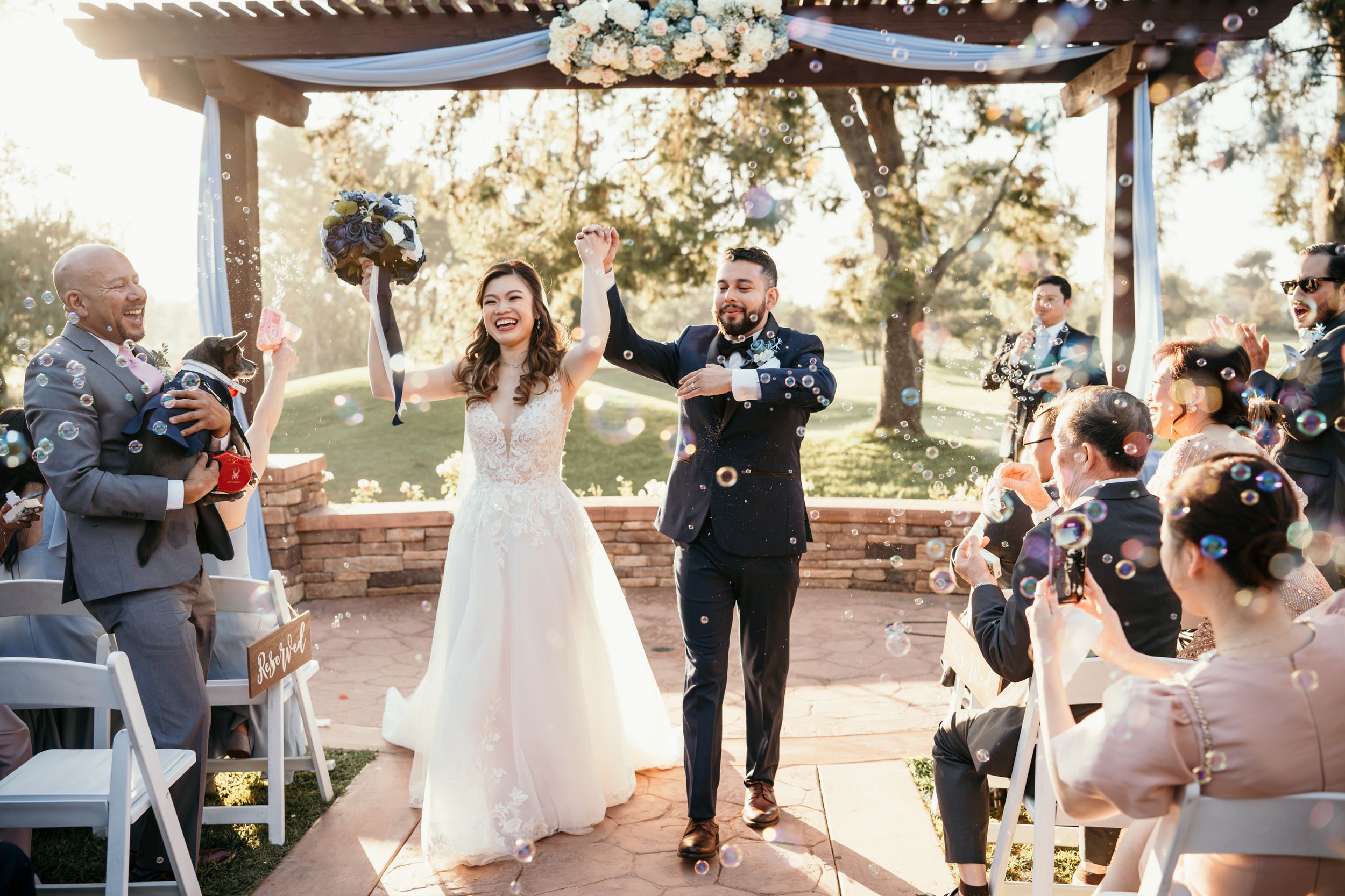 Newlyweds celebrating with raised arms during recessional at outdoor ceremony venue.