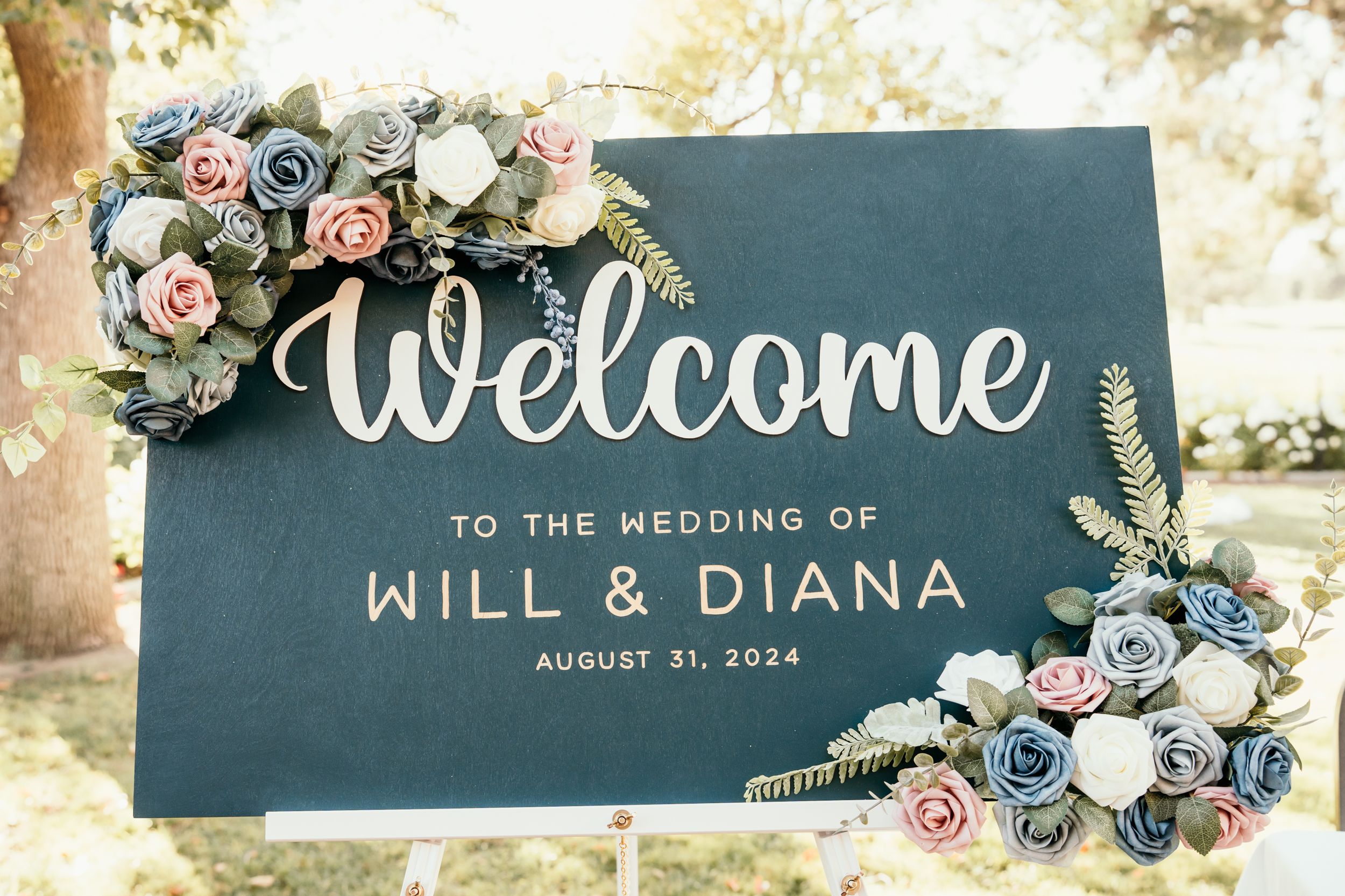 Navy blue welcome wedding sign decorated with blue and pink floral arrangements.