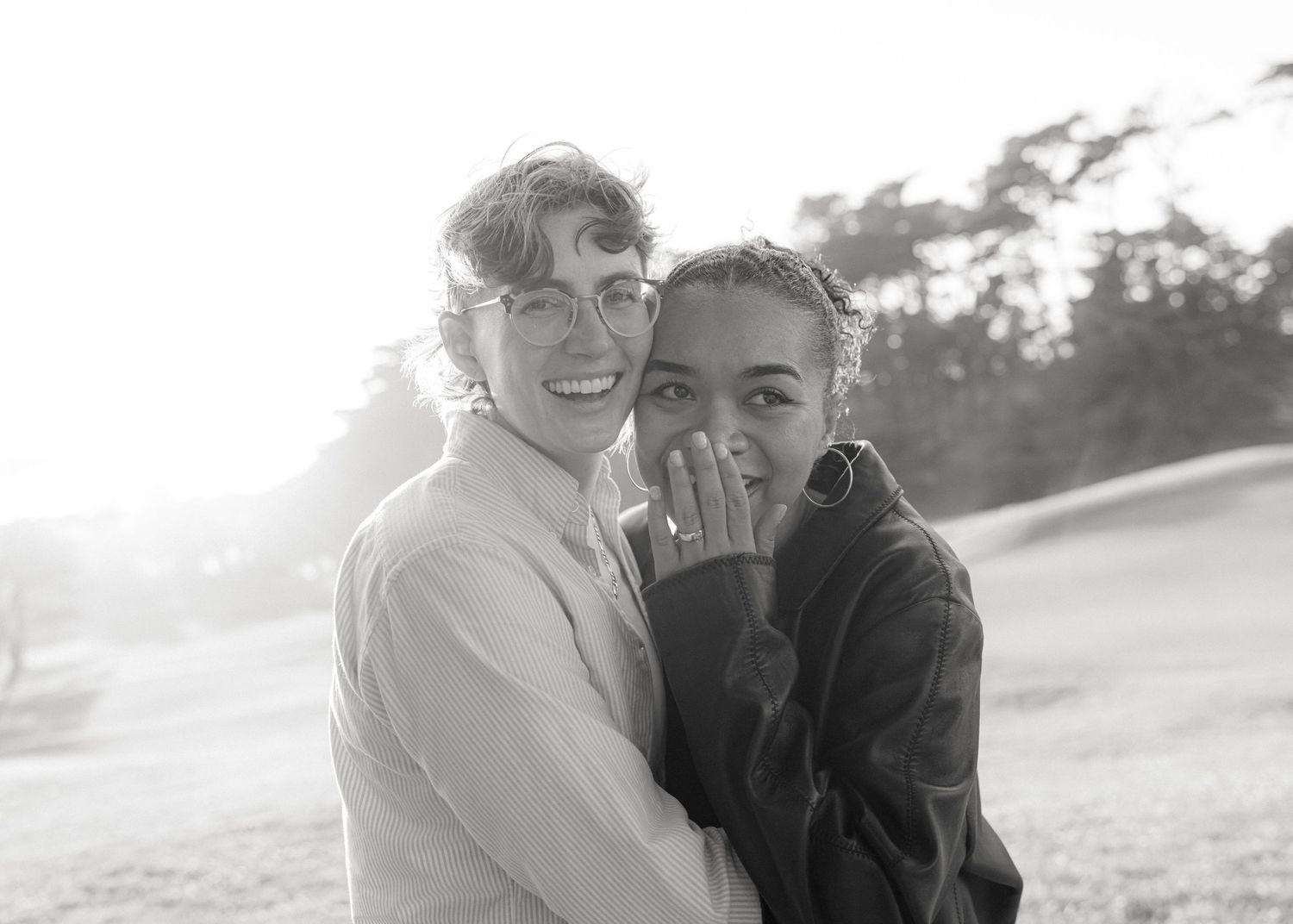 Two people share a joyful candid moment together outdoors in black and white photography.