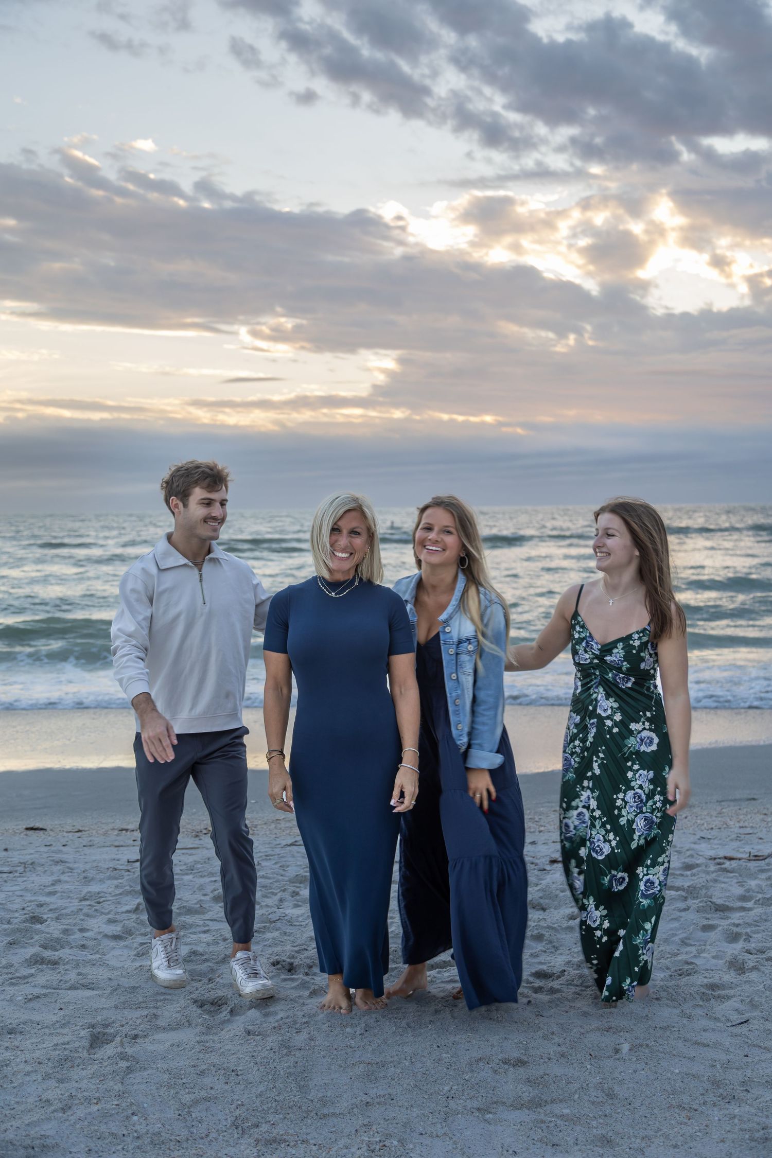 Family of four smiling on beach at sunset with ocean waves in background.