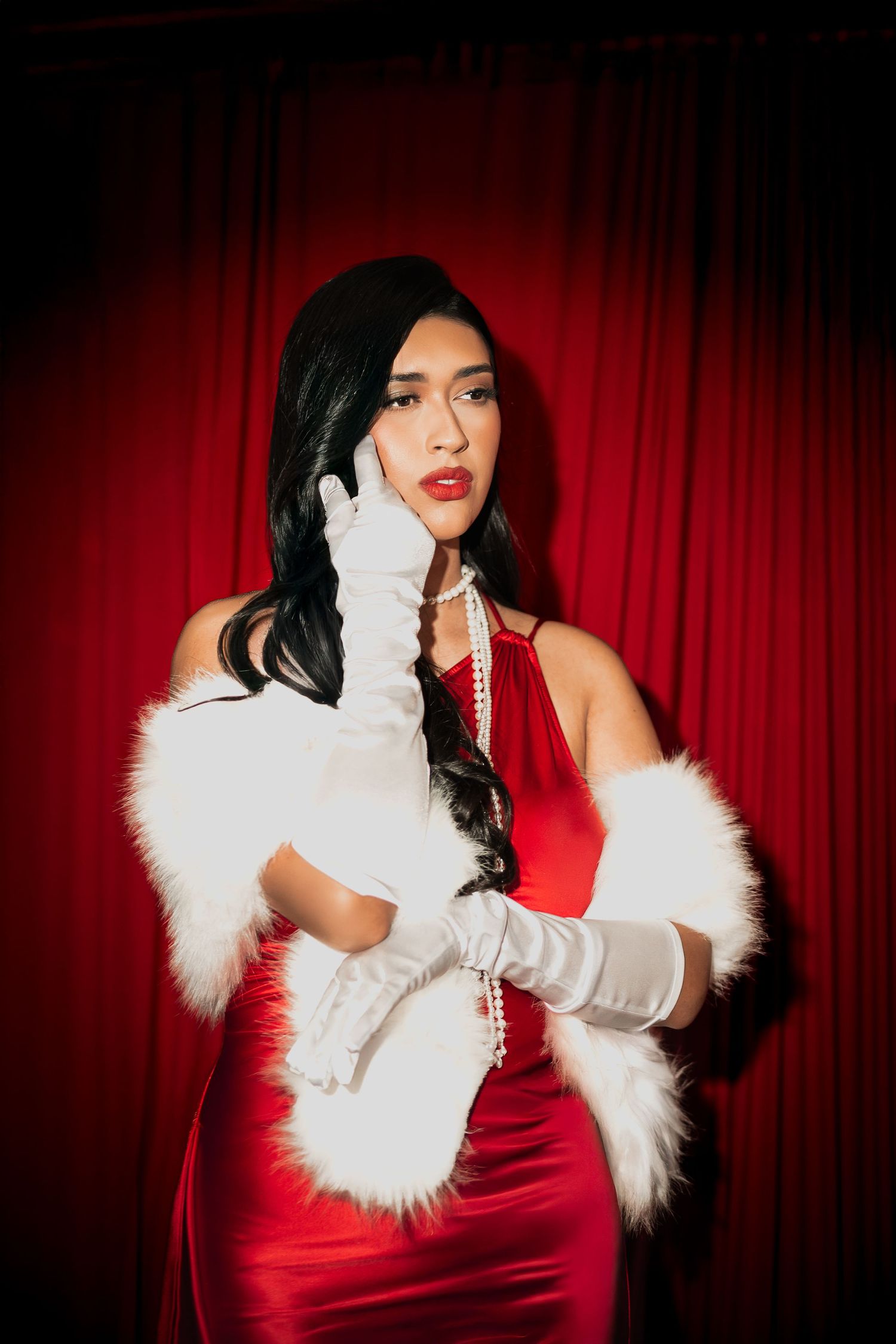 Vintage-inspired portrait with red dress and white fur against dramatic red curtain.