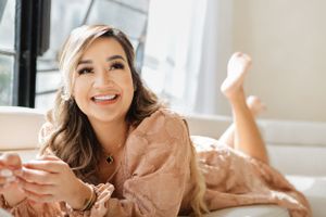 Relaxed figure in peach dress lying on white couch in sunny room.