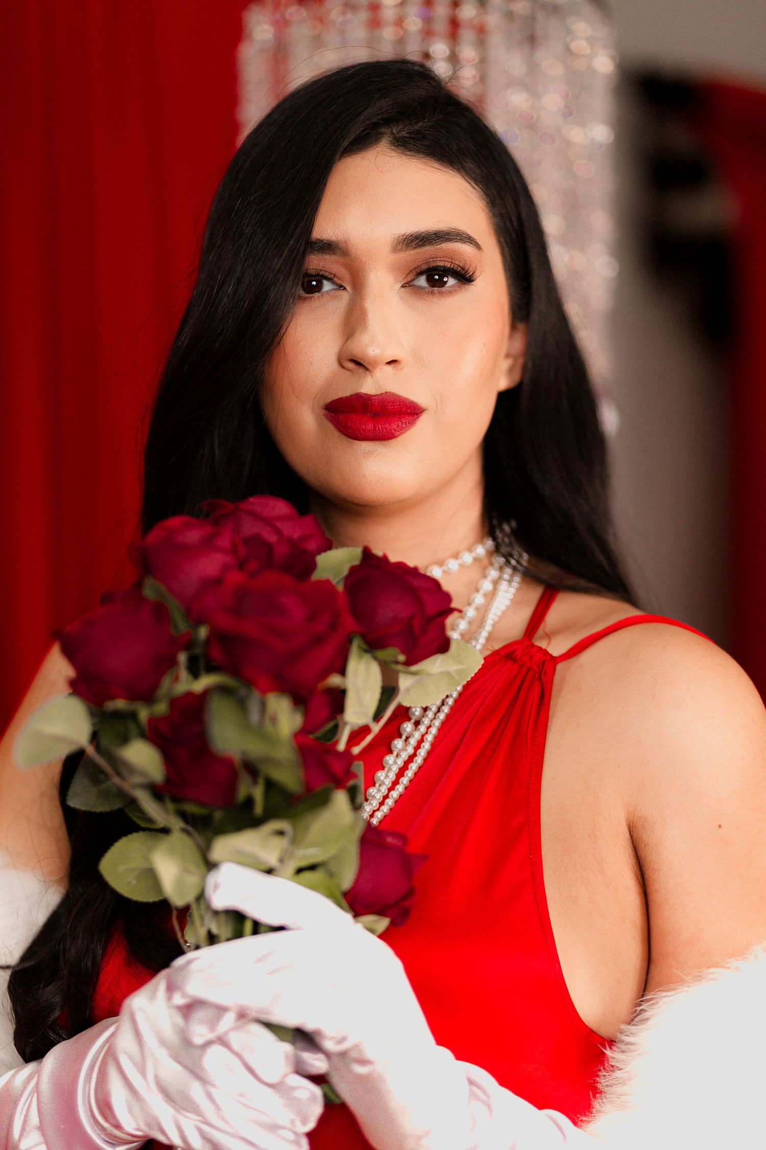 Glamorous portrait with red roses against crimson backdrop with crystal chandeliers.