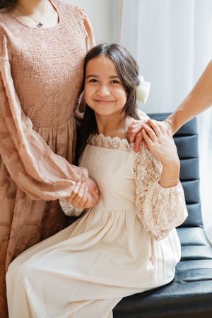 Two people in coordinating lace dresses sit together on dark furniture.