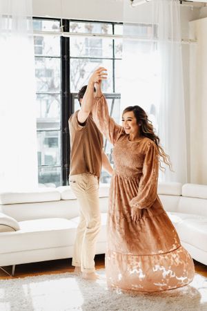 Couple dancing and twirling in coordinated outfits in bright white room.