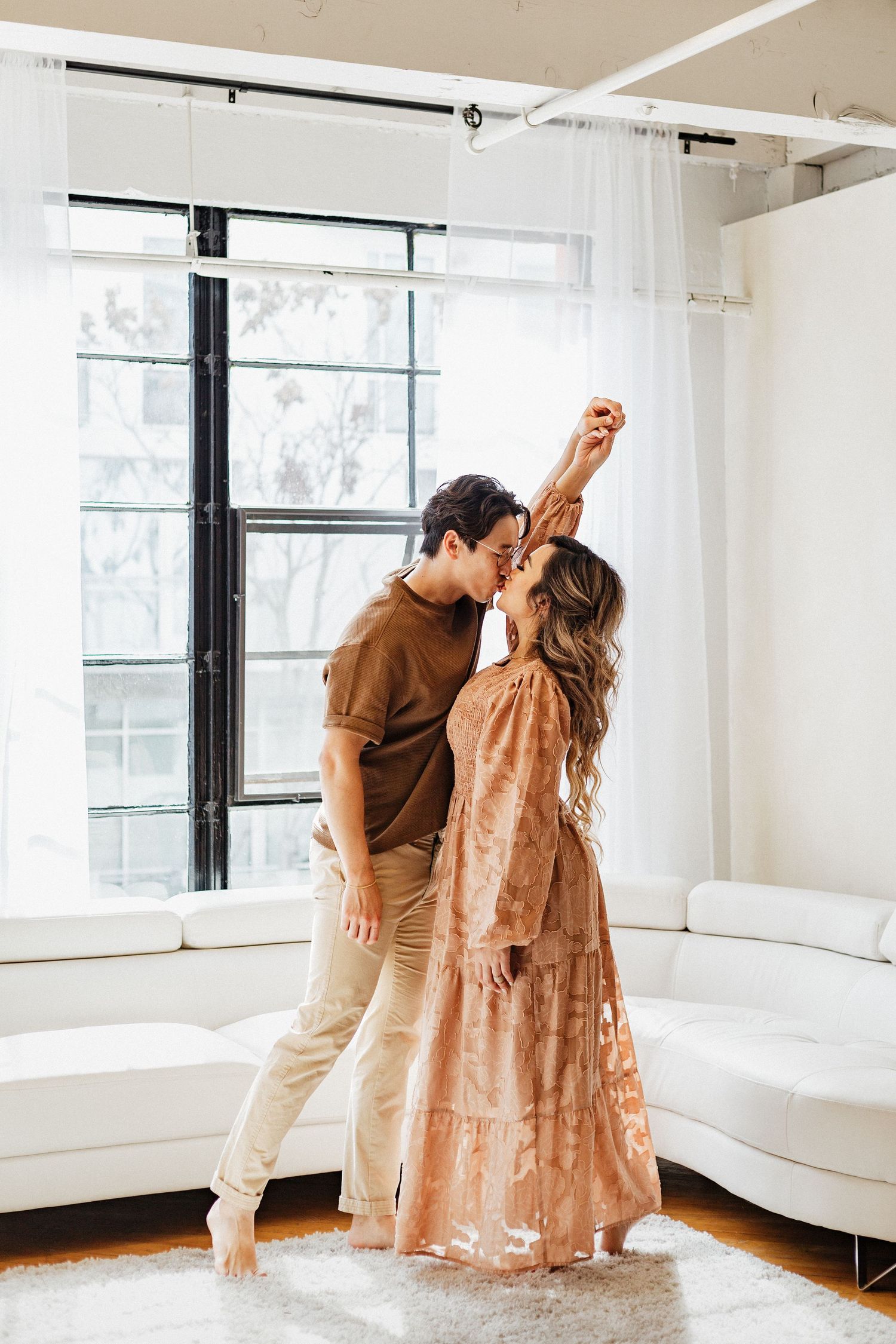 Couple sharing romantic dance moment in sunlit room with white decor.