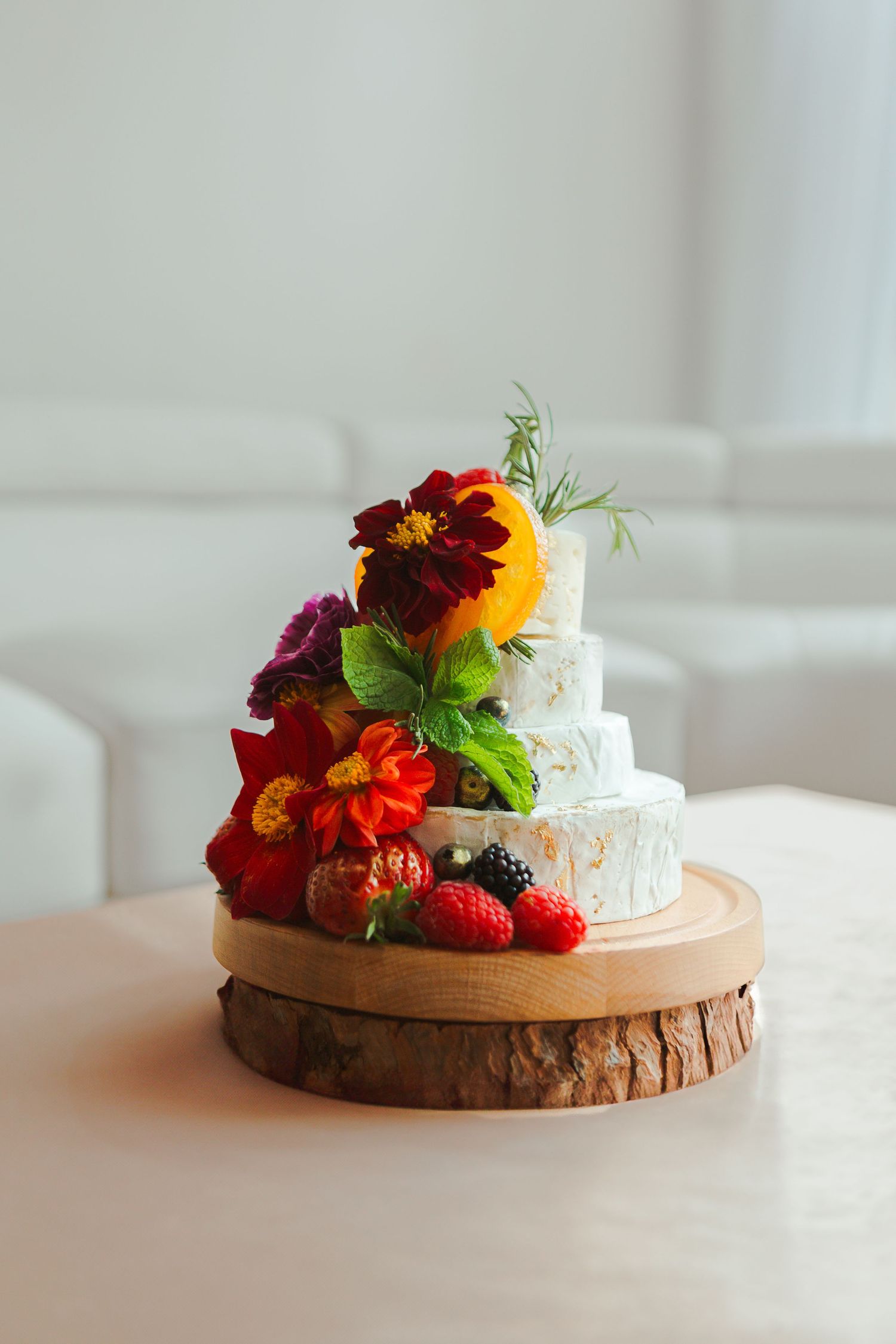 Small white wedding cake decorated with fresh flowers and berries on wooden stand.