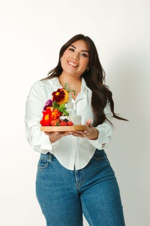 Woman in white button-up shirt holding colorful floral arrangement while standing against white wall.