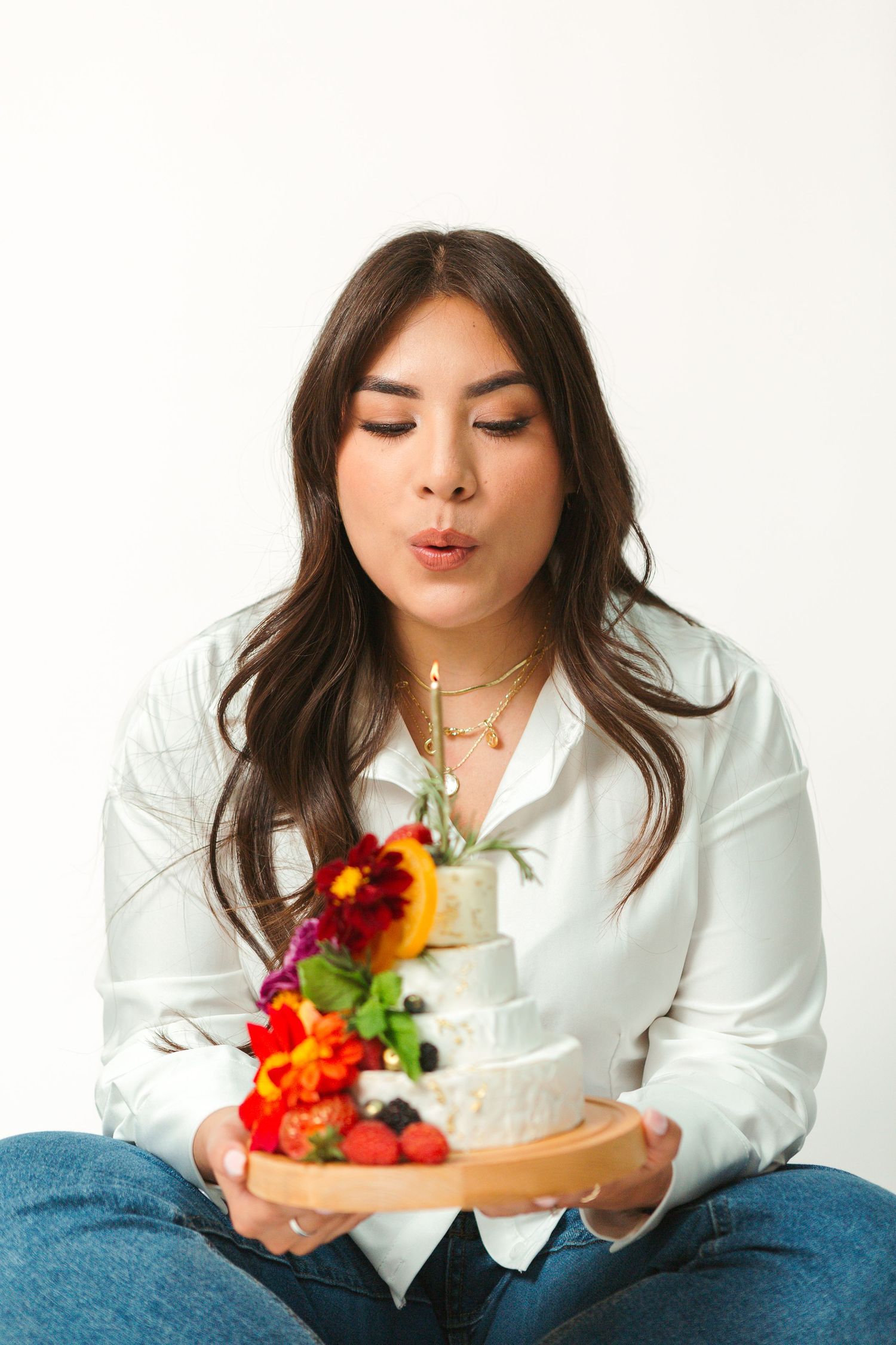 Woman in white shirt posing with decorative flowers against white backdrop.