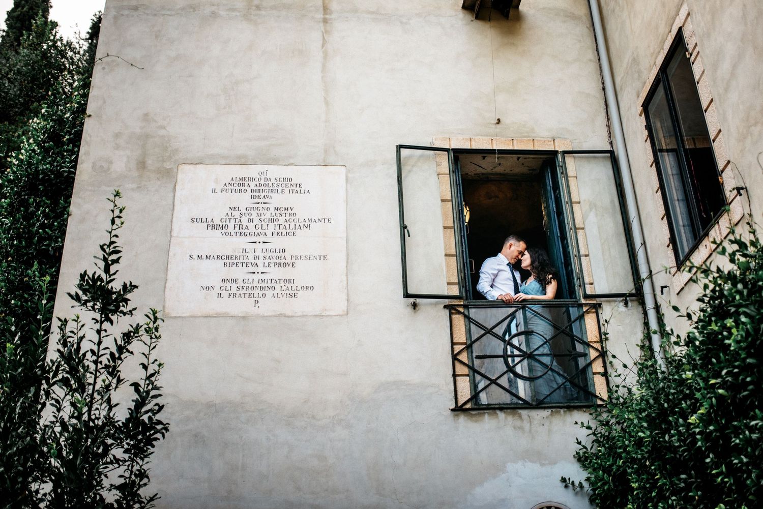 In home session of a couple in doorframe of their villa home while photographer takes a photo from the outside in Vicenza, Italy.