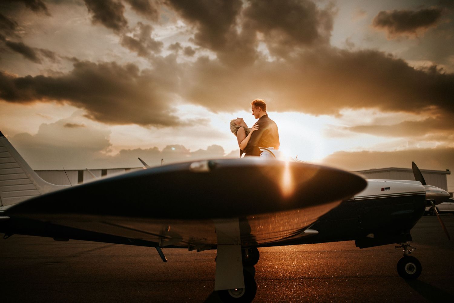 A couple laughing as they embrace on the wing of an airplane during a cloudy sunset with the sun flaring through in Clarksville TN.