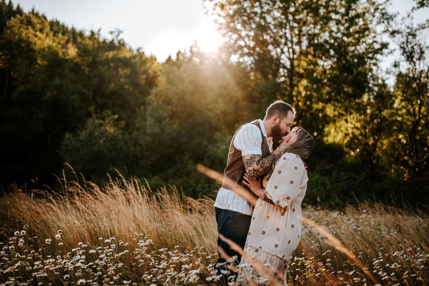 A couple sharing a kiss in a field with the sun setting behind the trees in Portland, Oregon.