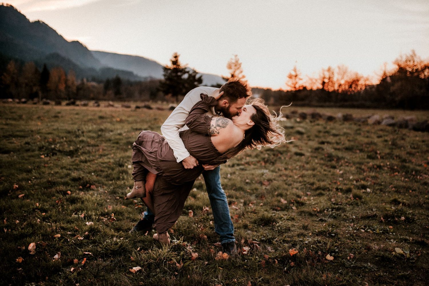 A couple dipping and kissing on an adventure in the gorge of Oregon with mountains behind them.