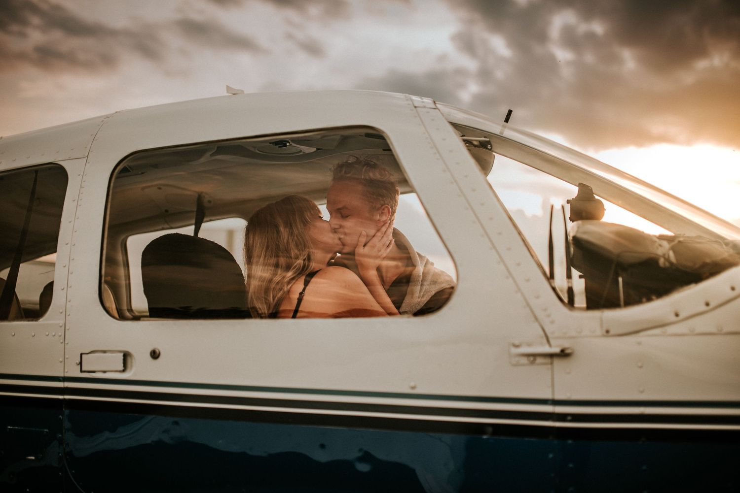 A couple sharing an intimate kiss in an airplane with the sunsetting behind them on a cloudy evening in Clarksville, TN.
