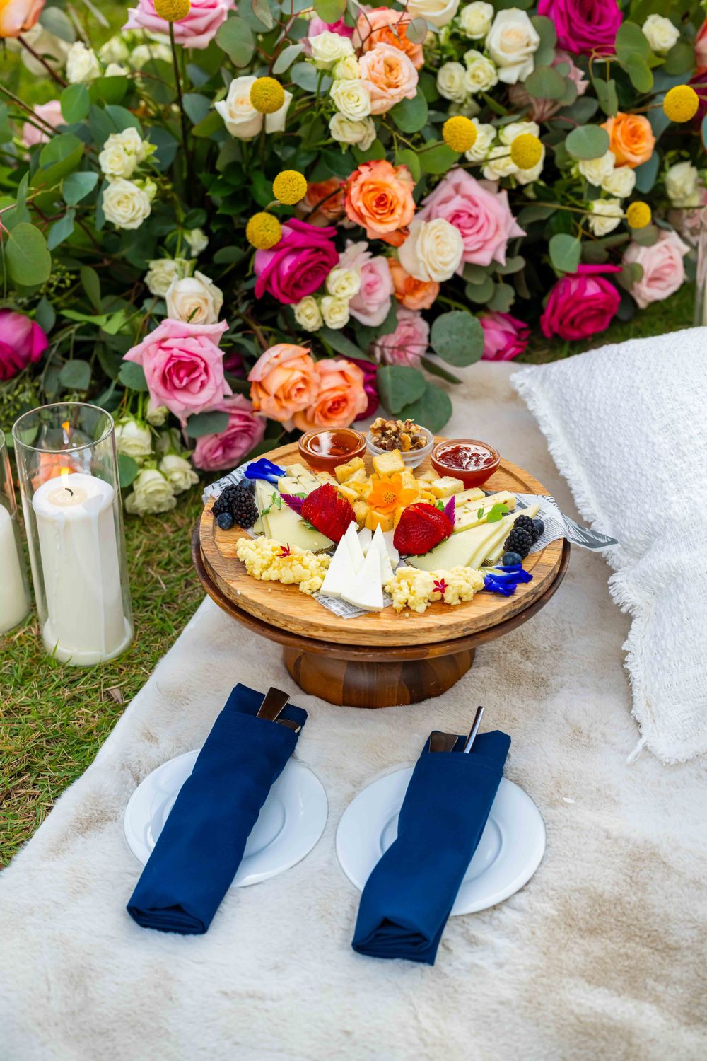 Elegant picnic setup with colorful floral display, charcuterie board, and navy blue napkins on white linen.
