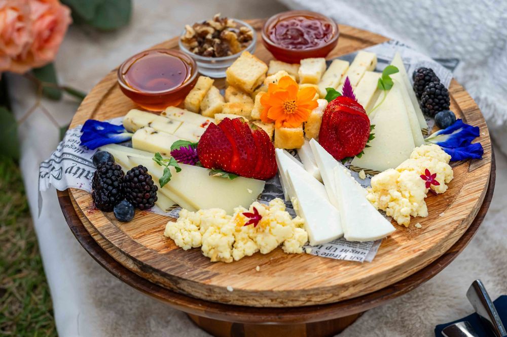 Wooden charcuterie board with assorted cheeses, fruits, nuts and jams arranged artfully.