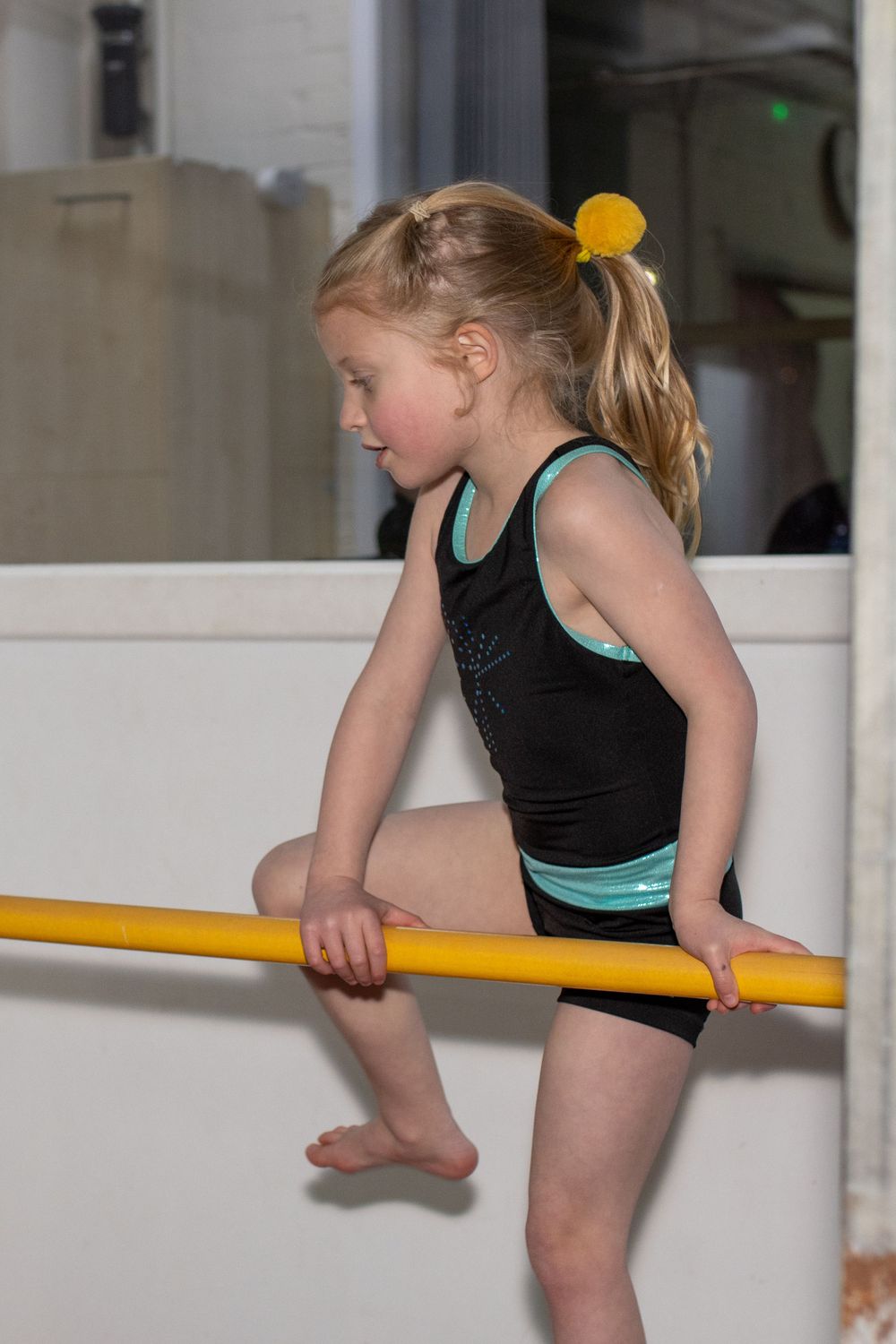 Young gymnast practicing balance exercises on a yellow beam in a training facility.