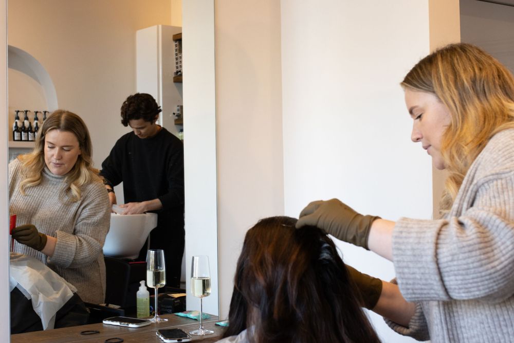 Busy salon interior showing styling stations and product displays along white walls.