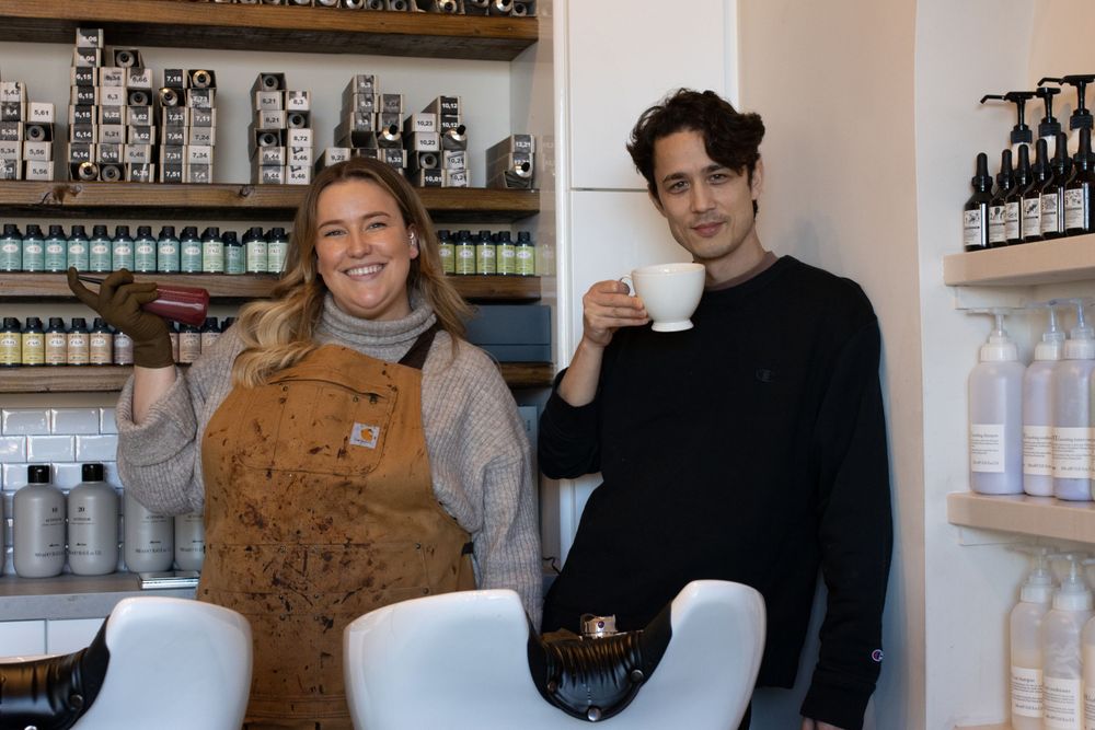 Salon staff members posing with beverages in front of product display shelves.