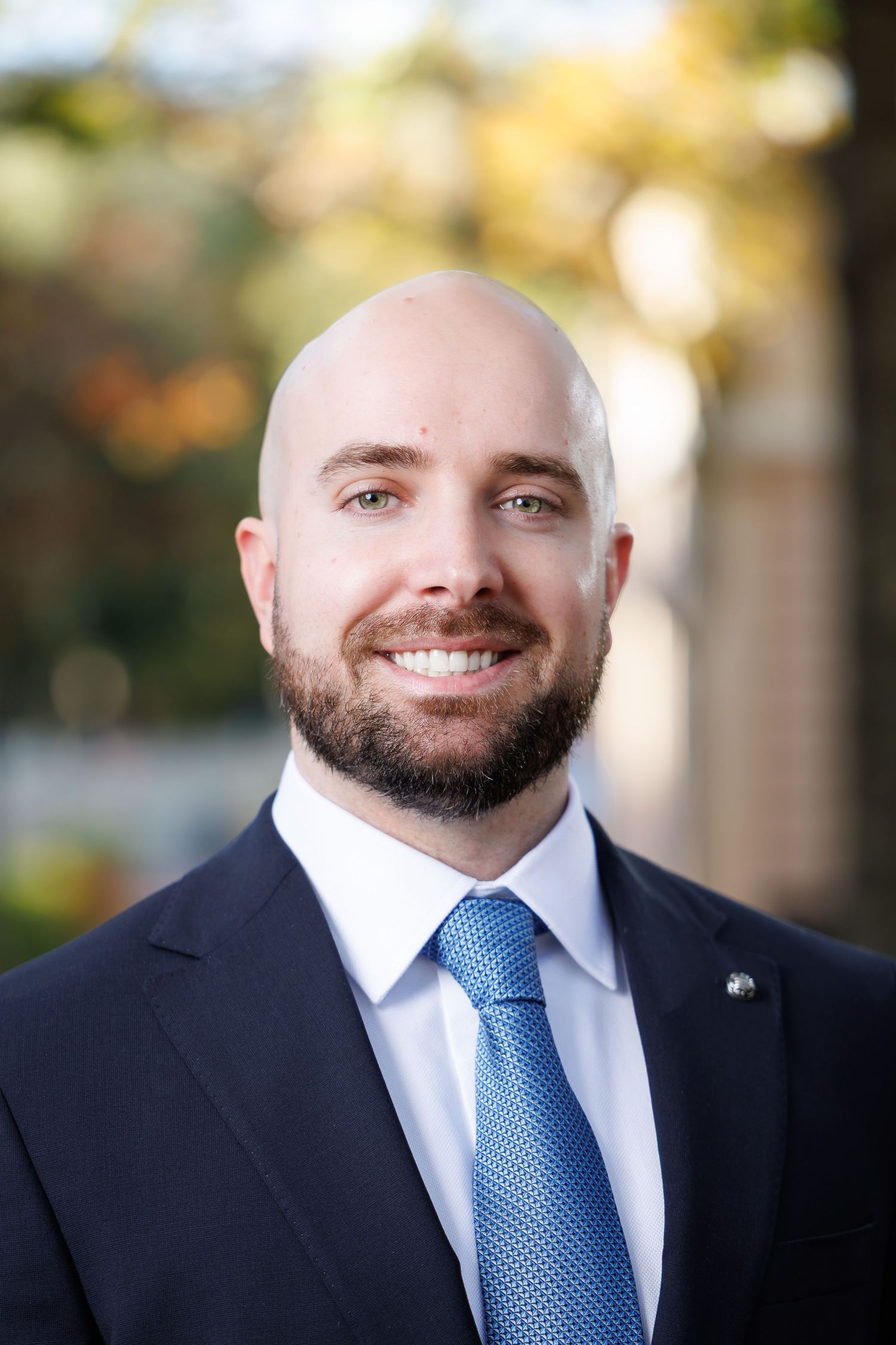 A smiling man wearing a blue suit and blue tie with a beard.